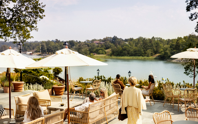 Personer njuter i solen på uteplatsen med utsikt över Hemviken