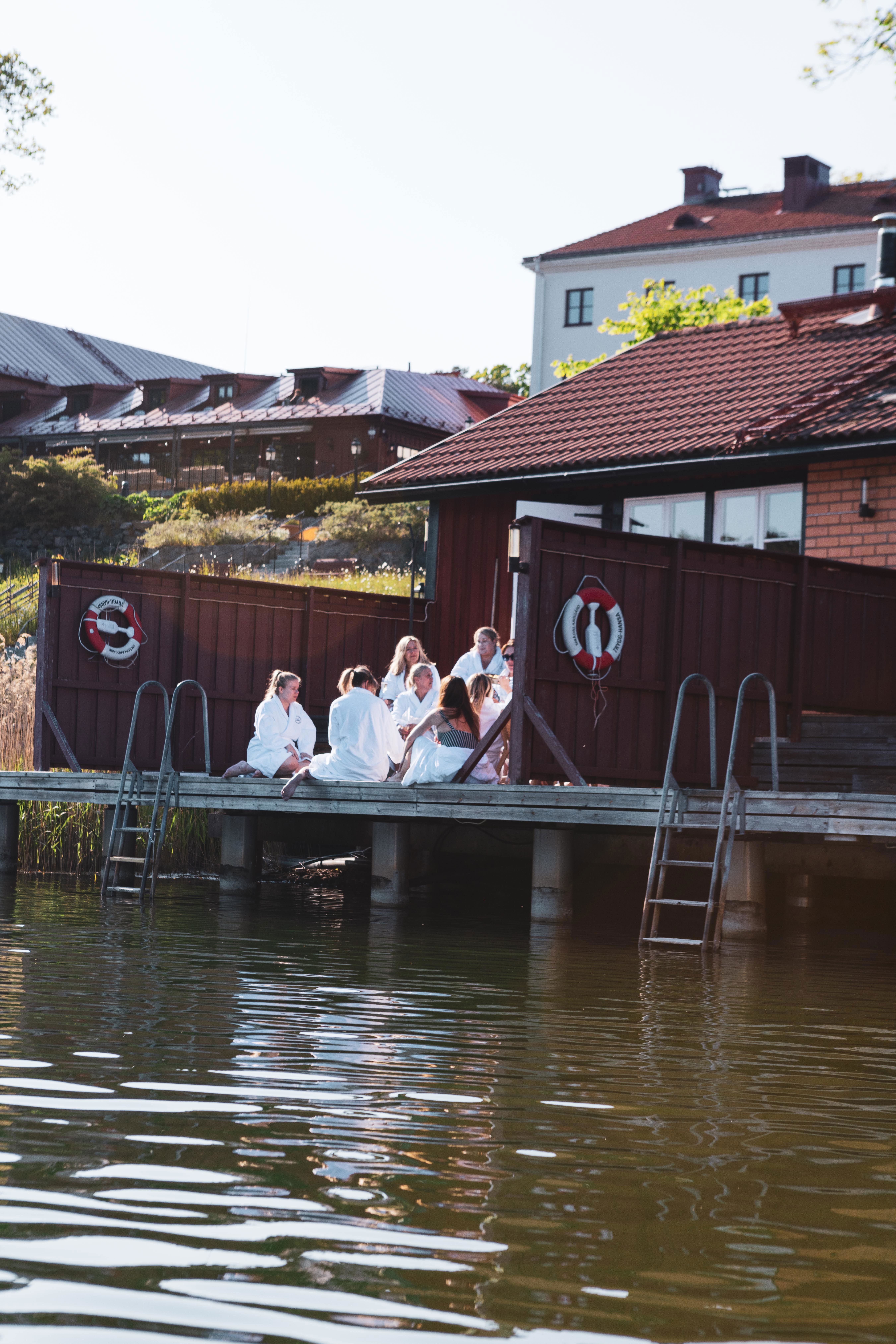 Människor sitter på altanen framför bastun som ligger i vattenbrynet