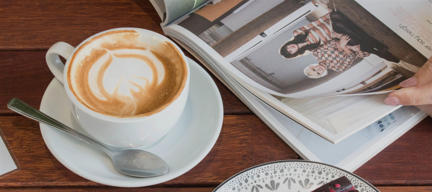 En person läser en livsstilstidning, drick kaffe och äter en bakelse