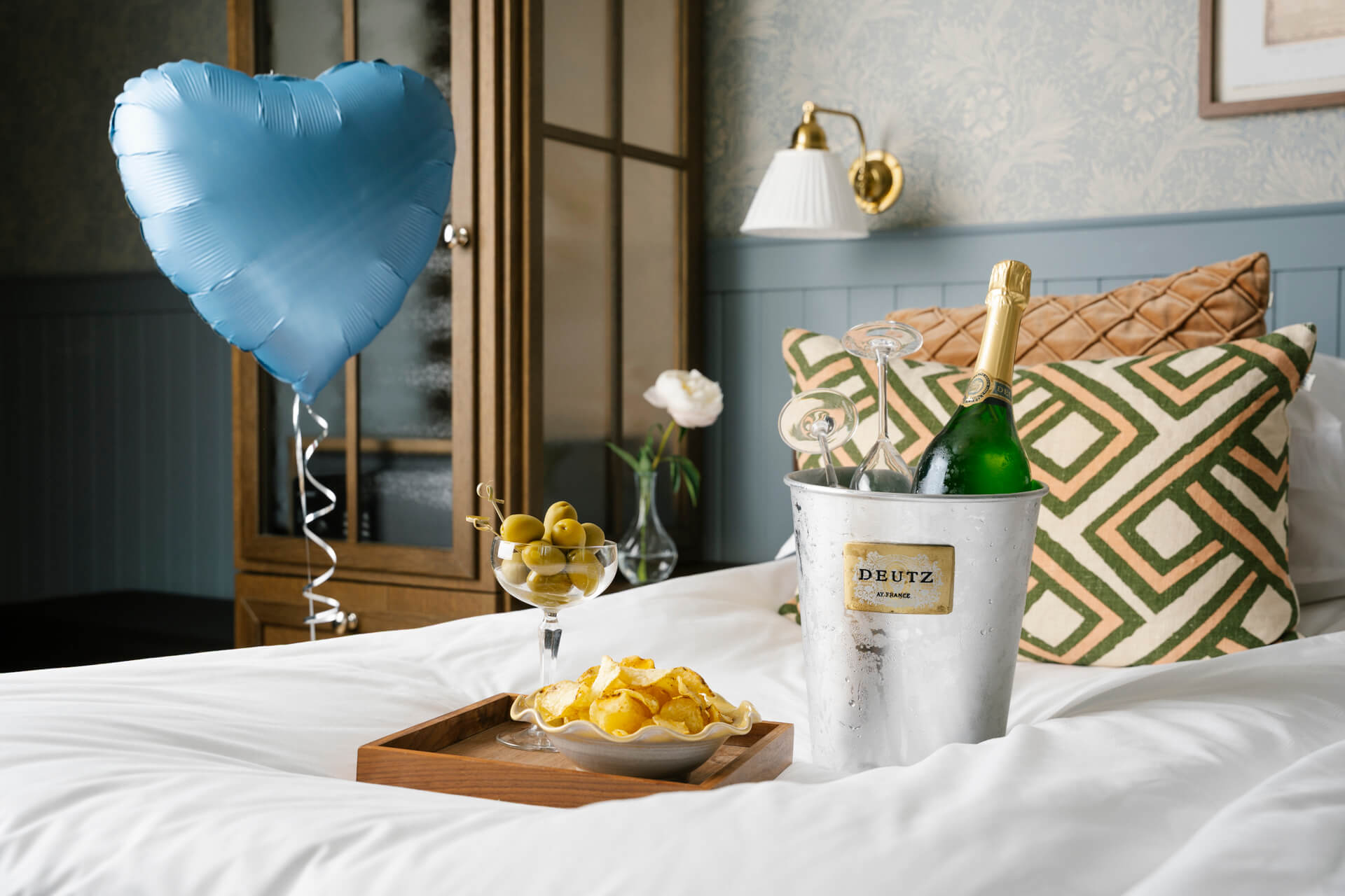 Champagne, snacks och en hjärtballong är placerad på hotellsängen