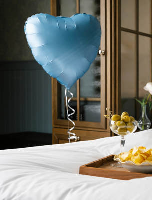 Champagne, snacks och en hjärtballong är placerad på hotellsängen