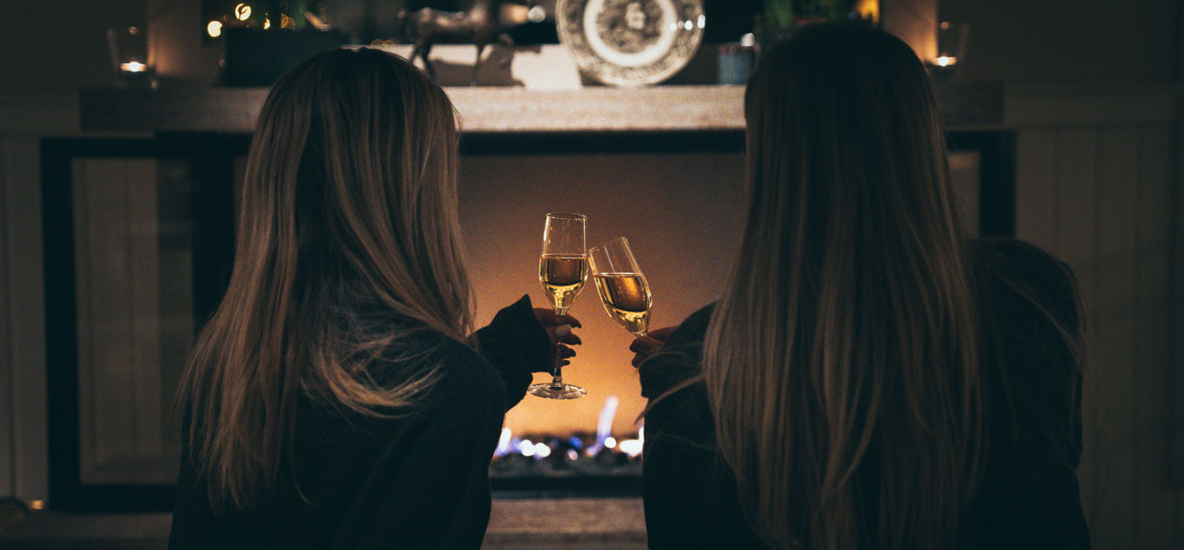 Två kvinnor skåla i champagne framför den öppna brasan