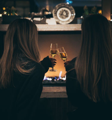 Två kvinnor skåla i champagne framför den öppna brasan